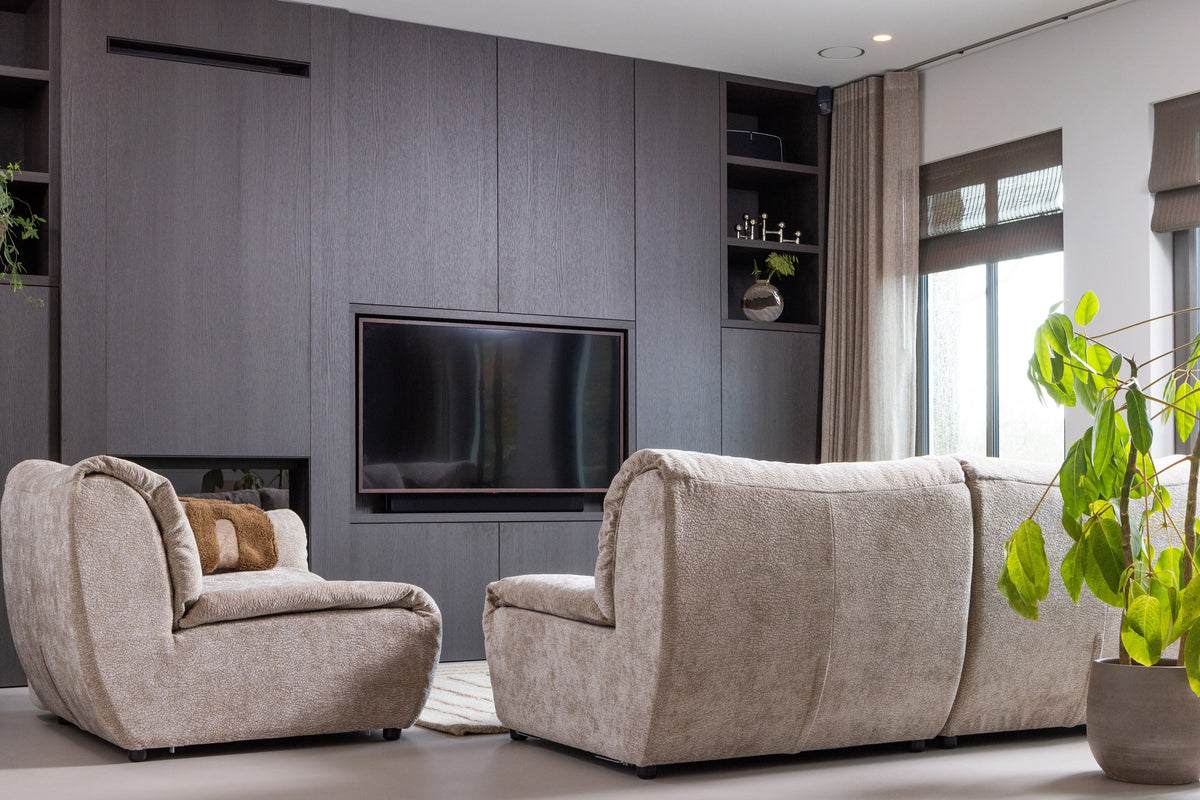 Baggy modulaire bankenserie in een zithoekopstelling, geplaatst voor een zwarte wandkast met tv en decoratieve items.